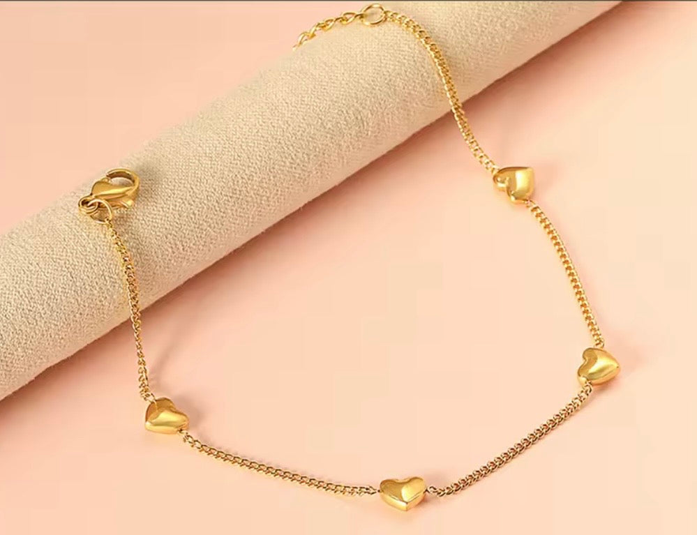 Gold hearts bracelet against light pink backdrop 