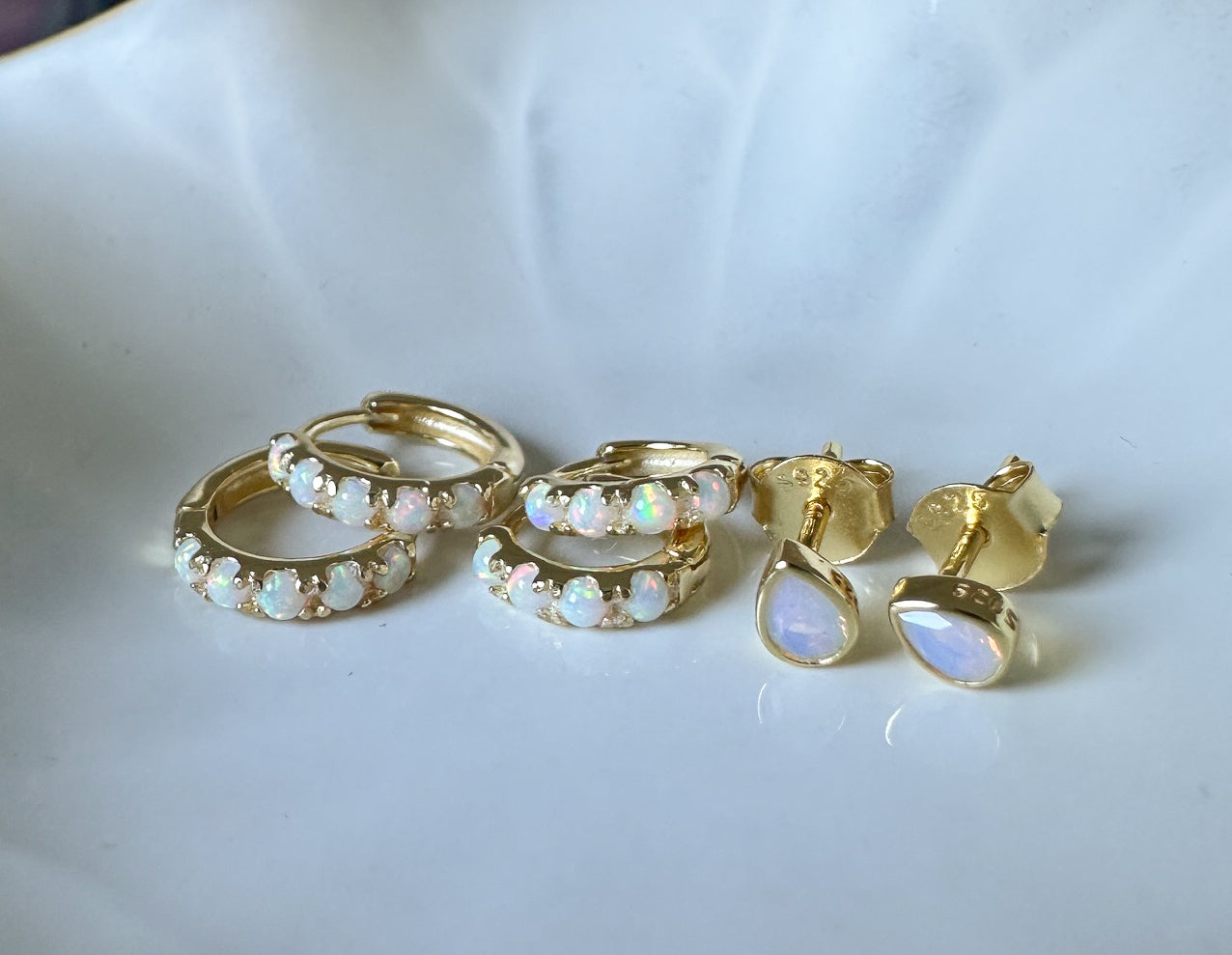 Gold hoop earrings with opal stones on a white surface