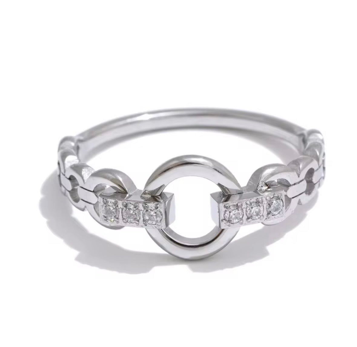 A silver-toned ring featuring a central open circle connected by chain-like segments, with small clear stones set along the sides, photographed on a white background.