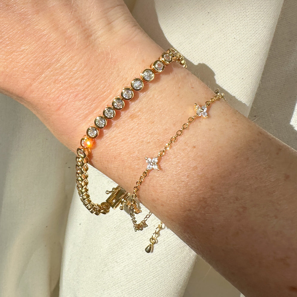 
                  
                    Gold  tennis bracelet with clear Cubic zirconia bezel set stones on a wrist against a neutral background
                  
                