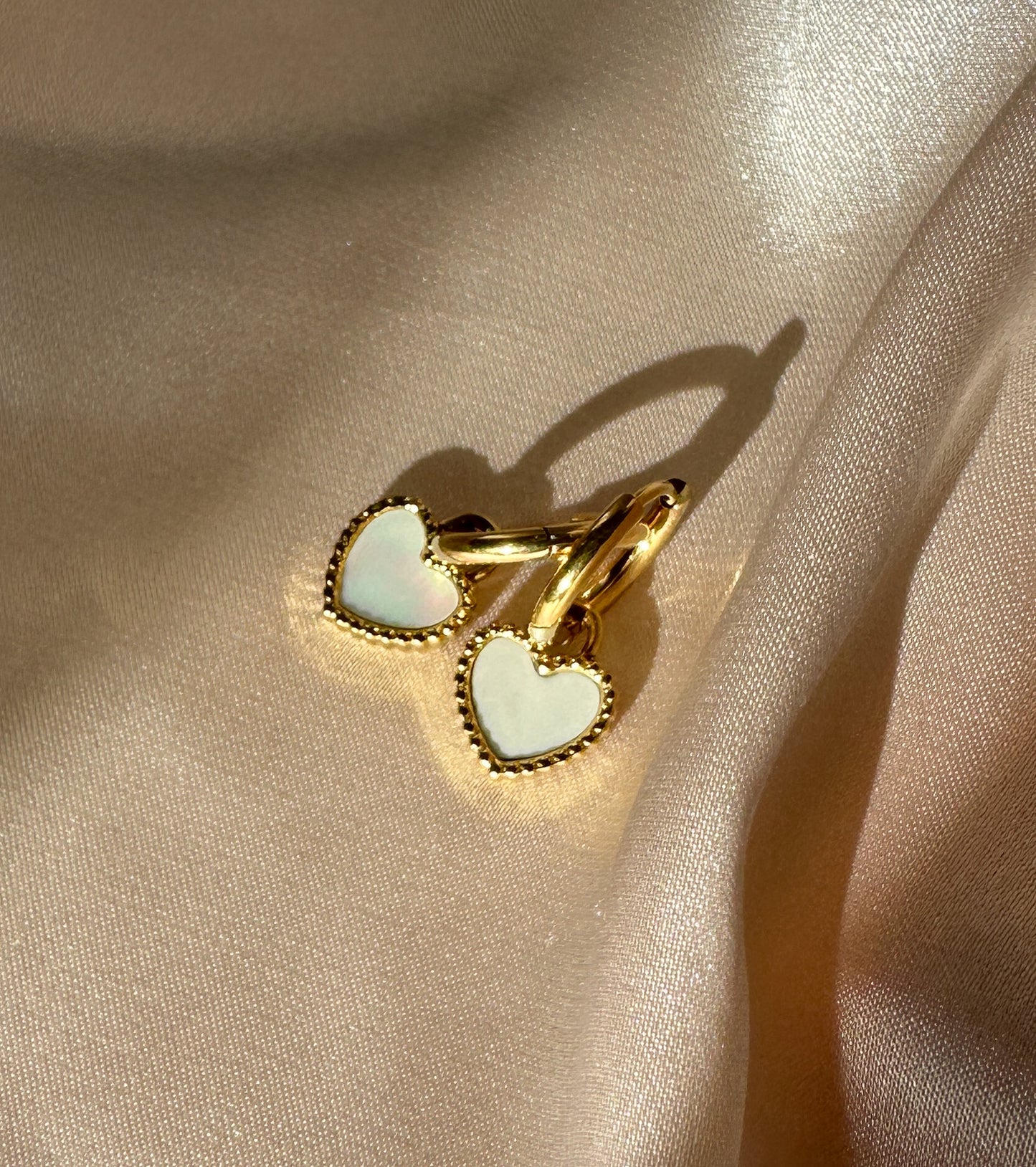 Heart-shaped earrings with gold beaded edging and white center on beige fabric