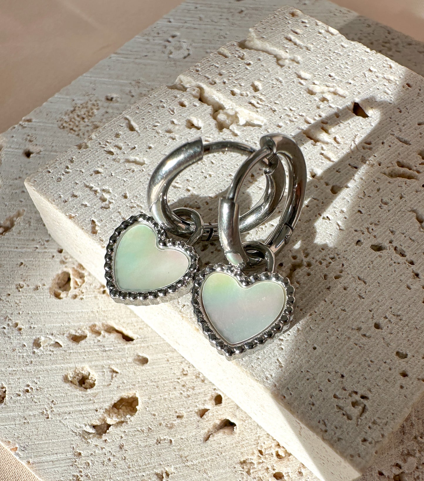 Silver heart-shaped earrings on a textured stone surface