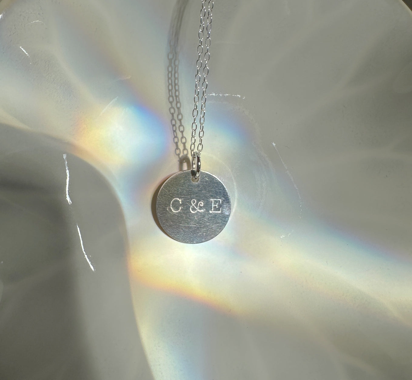 Silver necklace disc necklace with hand stamped initials on a white ceramic dish