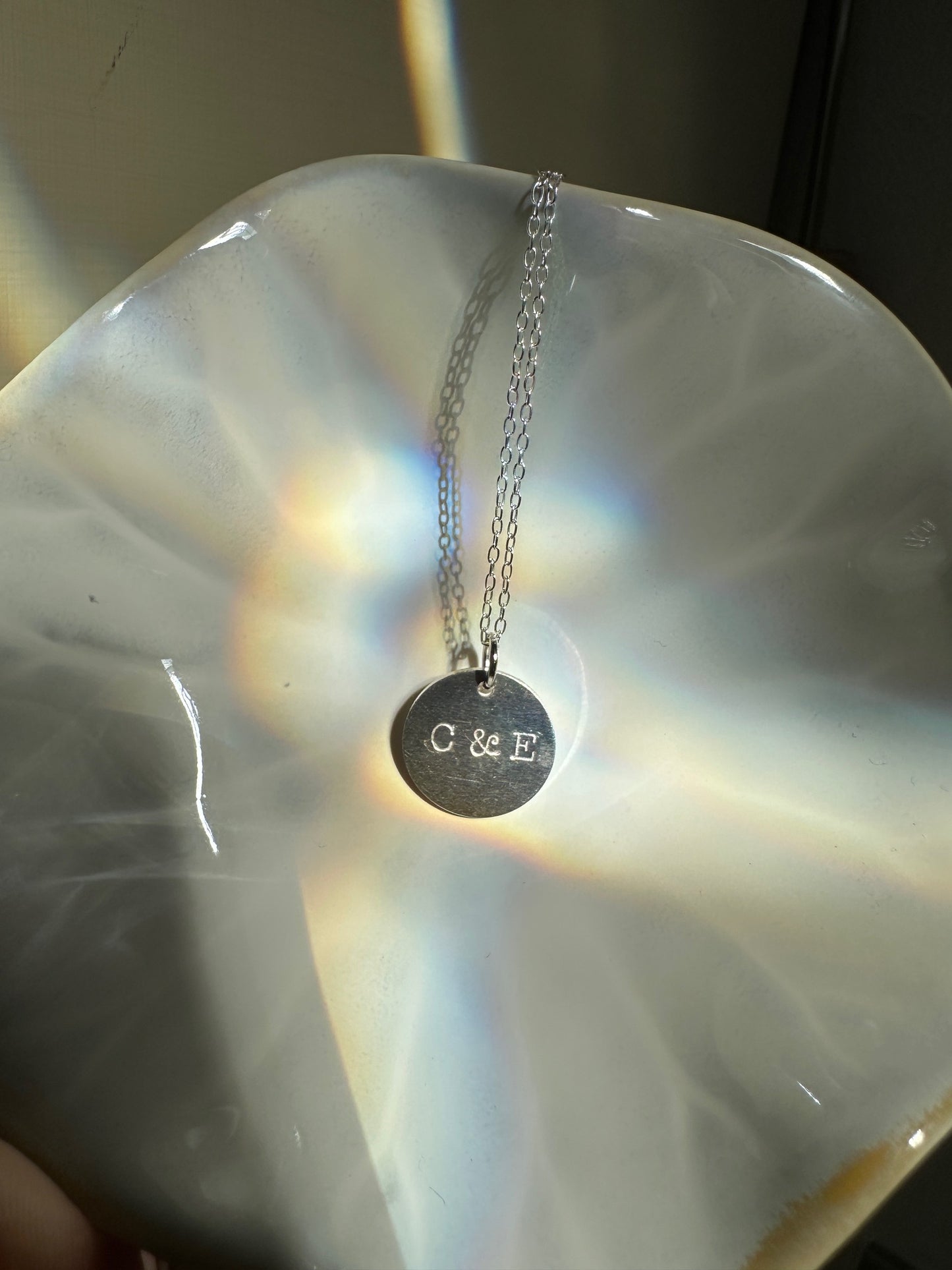 Silver necklace disc necklace with hand stamped initials on a white ceramic dish