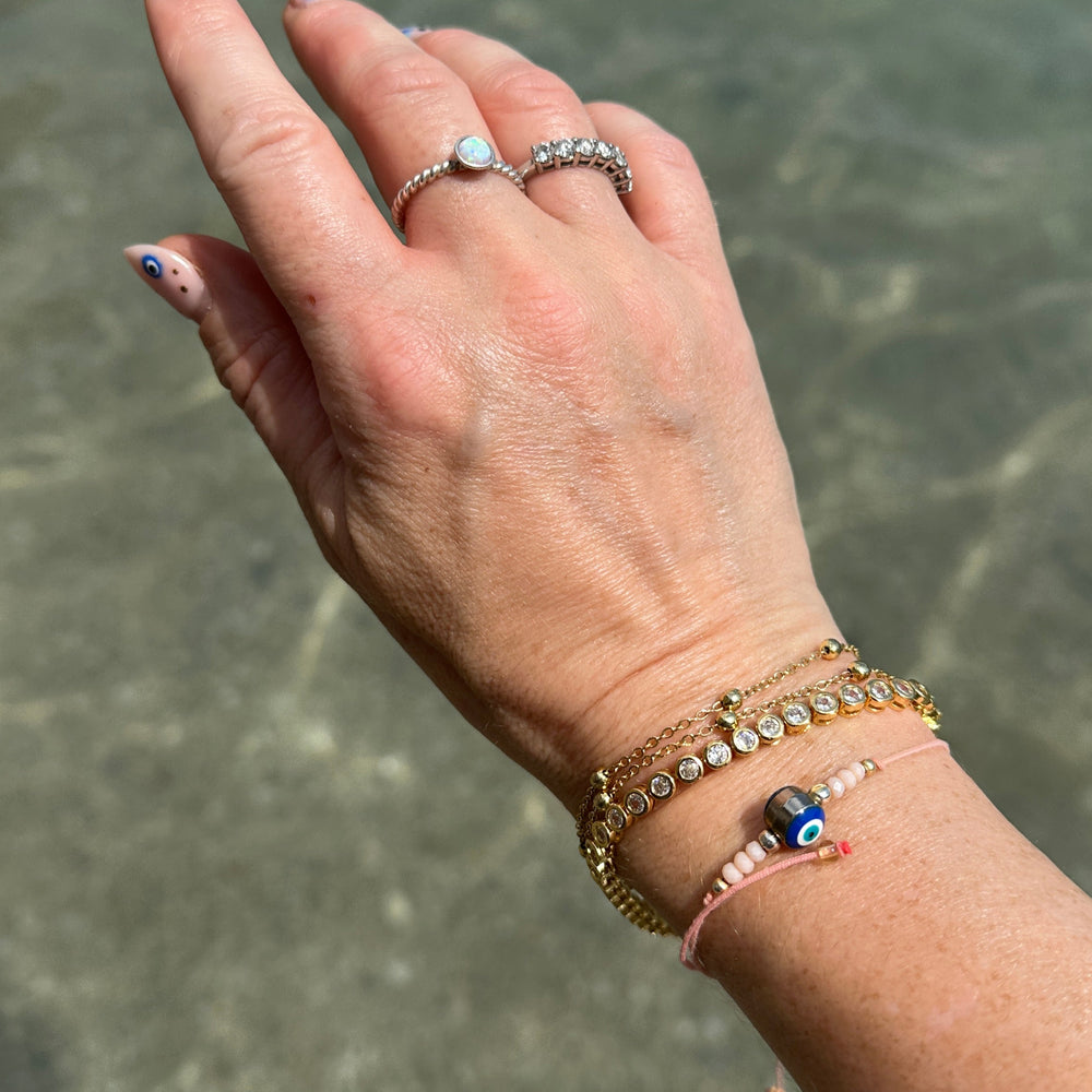 
                  
                    Gold tennis CZ bezel set bracelet as part of a wrist stack against clear ocean backdrop modelled on a hand
                  
                