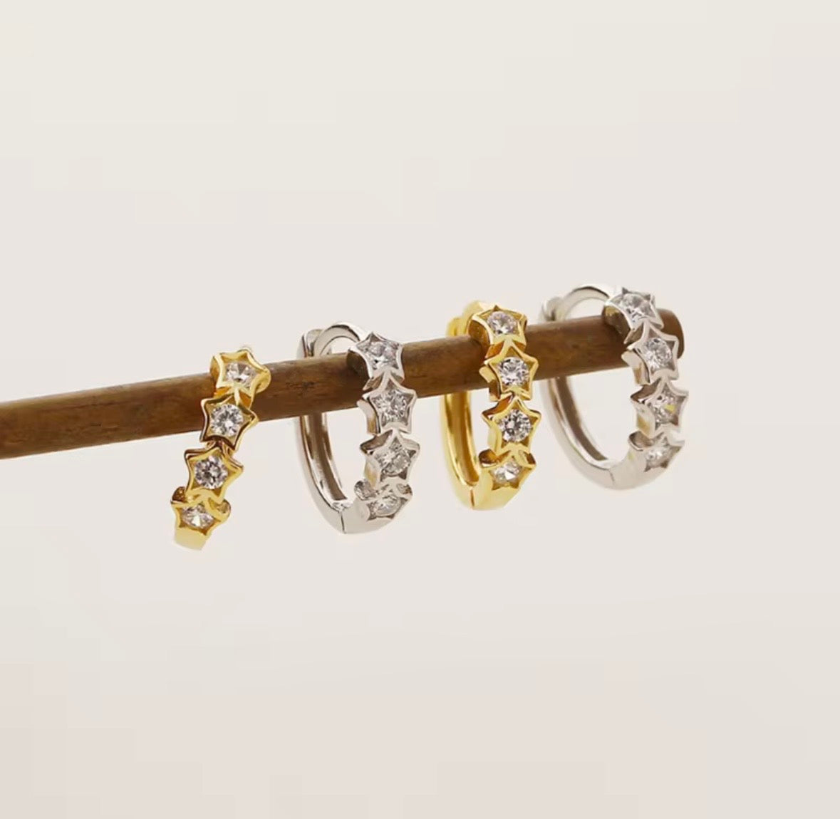 Set of tiny  gold and silver star huggie hoop earrings on a wooden stick against a light background