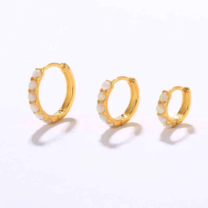 Set of gold hoop earrings with white opals on a light gray background
