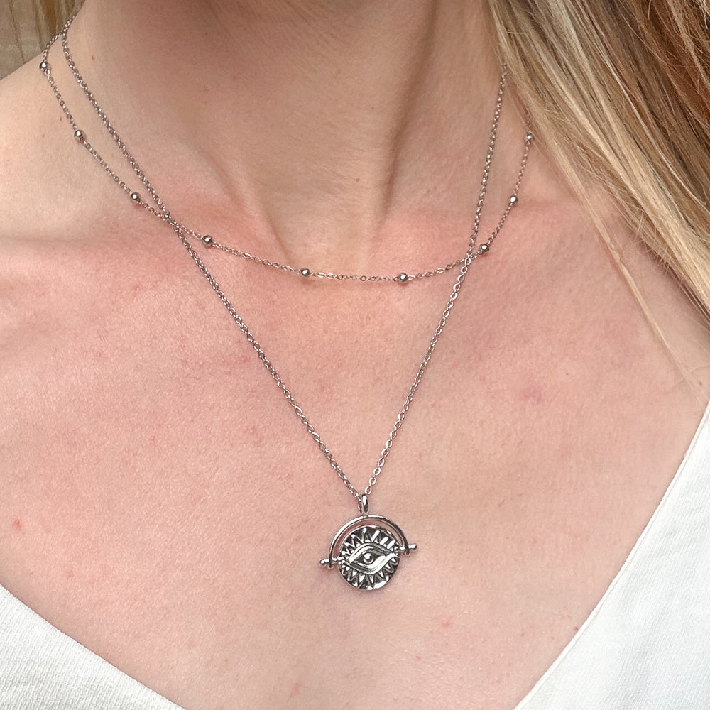 
                  
                    Silver evil eye necklace with a pendant worn by a person
                  
                
